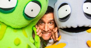 A man poses with three colorful stuffed animals, featuring green and yellow designs, showcasing a playful atmosphere.