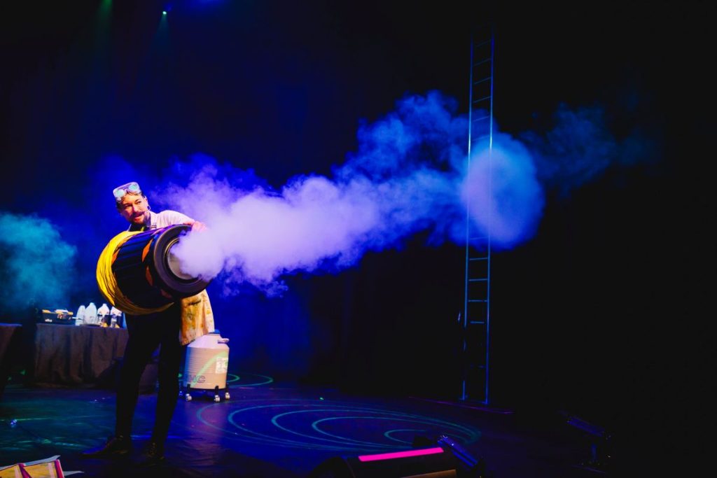 A man performing on stage, exhaling smoke dramatically, creating an intense atmosphere.