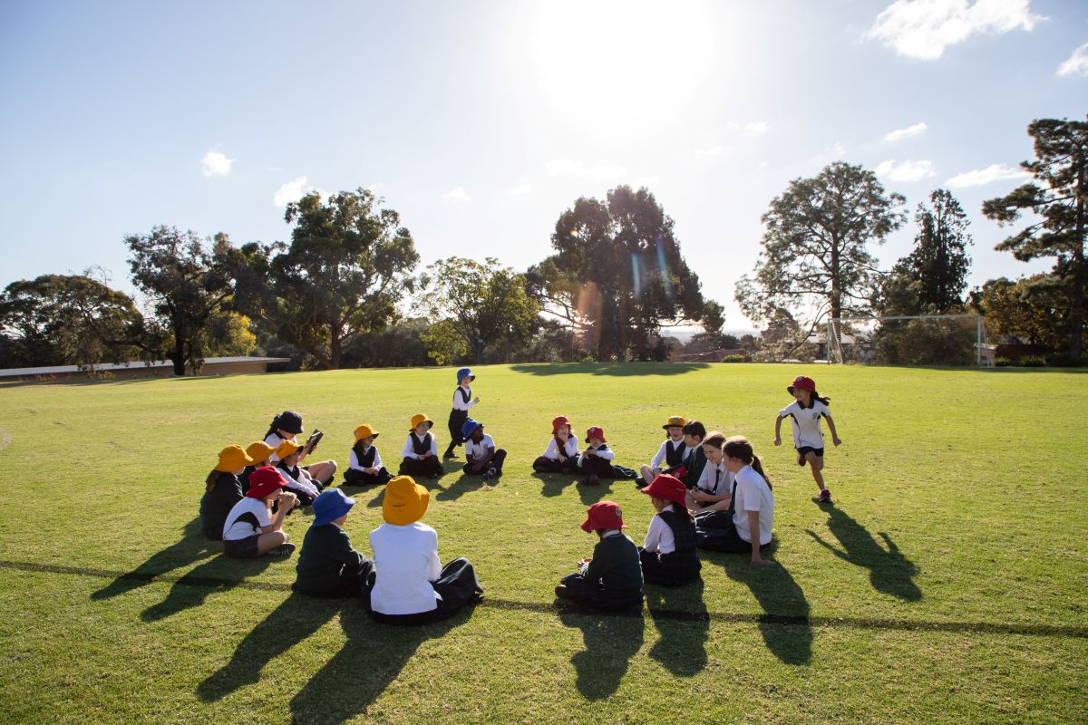 A group of children sitting in a circle on the grass, engaged in play and enjoying a sunny day outdoors.