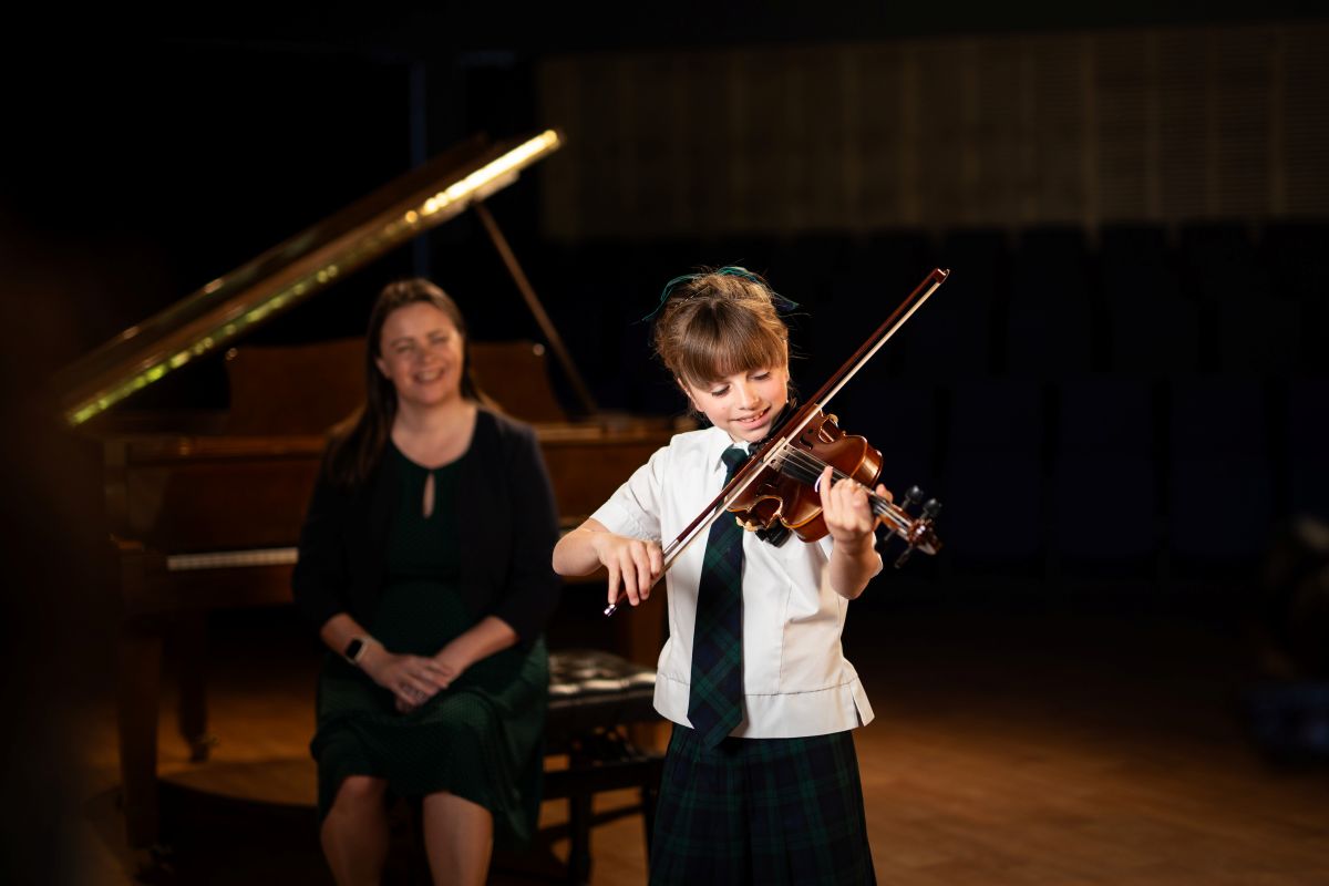 A young girl in a school uniform joyfully playing the violin, showcasing her musical talent and passion for music.