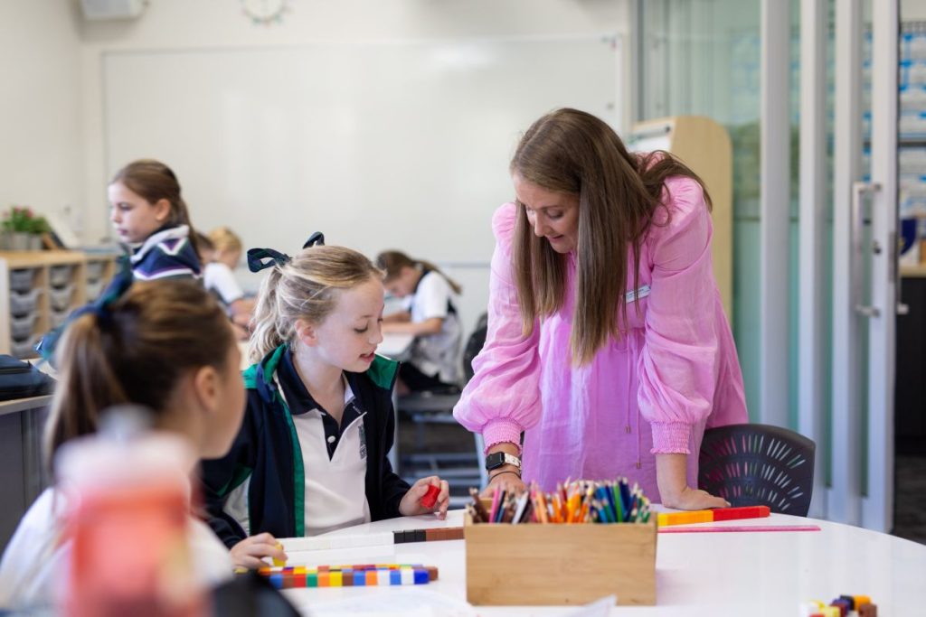 A teacher assists students with their assignments in a bright, engaging classroom setting.