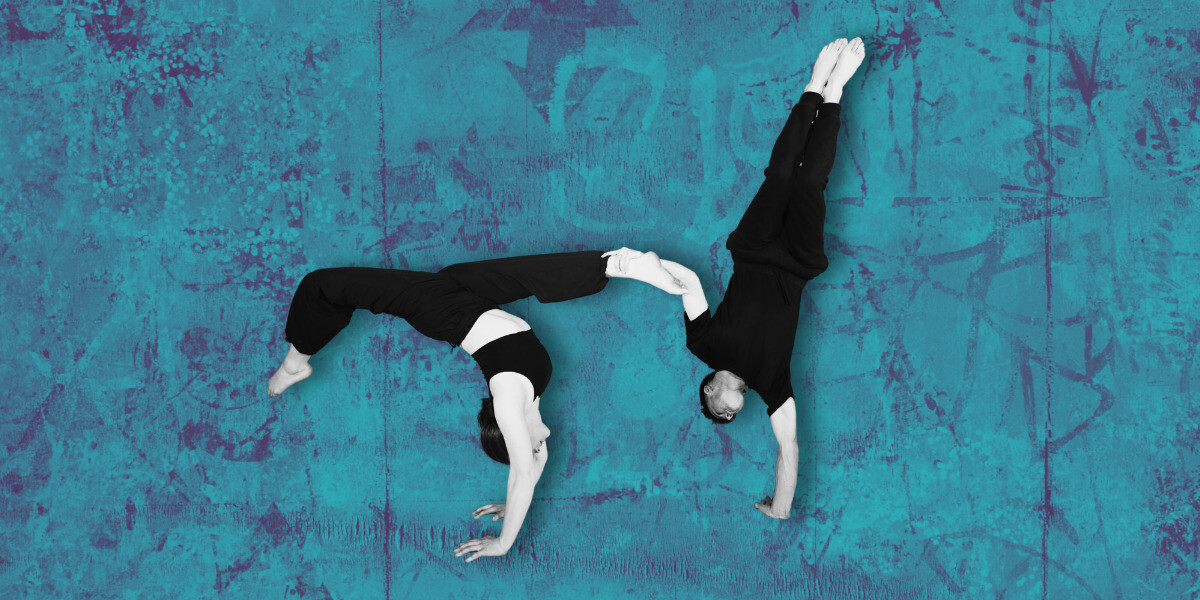 Two acrobats performing impressive moves against a vibrant blue wall.