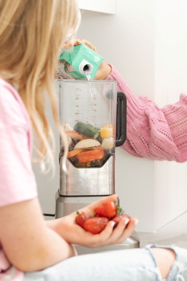 A woman pours water into a blender, preparing ingredients for a smoothie or other blended drink.