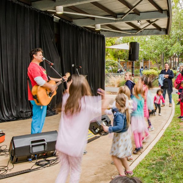 A group of children joyfully performing on stage while a man plays guitar, creating a lively and fun atmosphere.