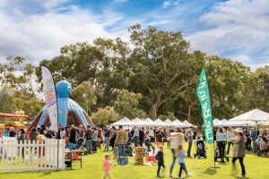 A diverse crowd gathers at an outdoor event, enjoying the atmosphere and activities under a clear blue sky.