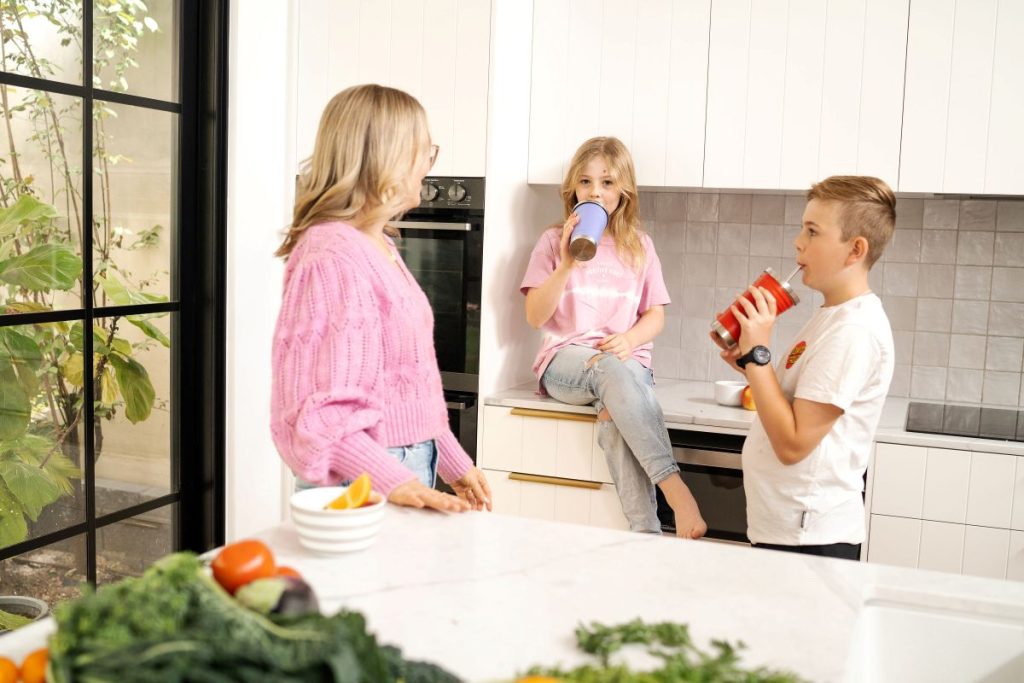 Two young girls and a boy in a kitchen, surrounded by fresh vegetables, engaged in cooking together.