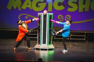 A magician performs tricks at a vibrant magic shop, captivating an audience with illusions and colorful props.