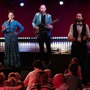 A group of people on stage, with a man playing guitar, creating a lively musical atmosphere.