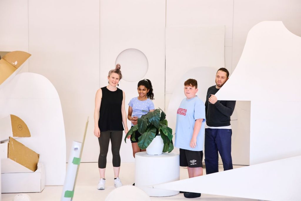 Three individuals pose together in front of a plain white wall, smiling and enjoying their time.