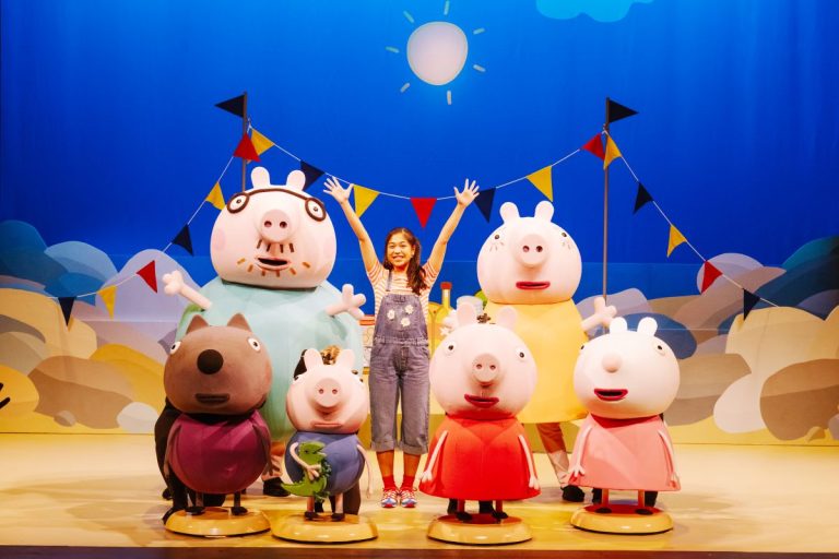 A woman stands smiling in front of several colorful Peppa Pig characters, creating a cheerful scene.