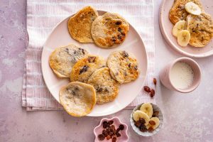 A plate of fluffy pancakes topped with sliced bananas and sprinkled with raisins.