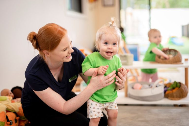 A woman sits on the floor, holding a baby in her arms, both appearing calm and content.