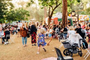 A diverse crowd of people gathered at an outdoor event, enjoying activities and socializing under a clear blue sky.