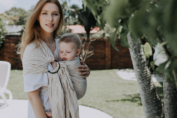 A woman holds a baby in a carrier, smiling gently as they share a moment together.