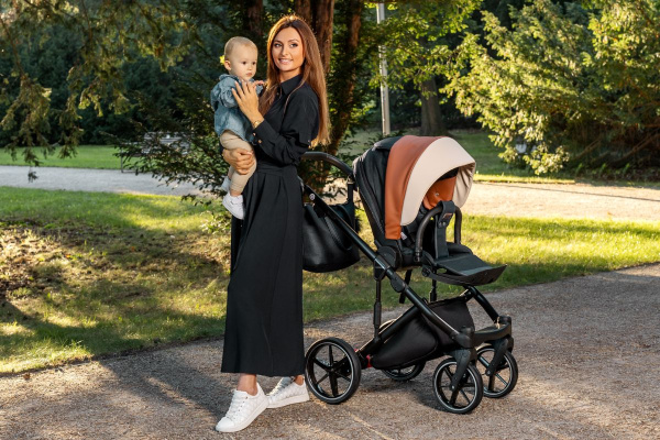 A woman gently holds her baby in a stroller while smiling in a sunny park.