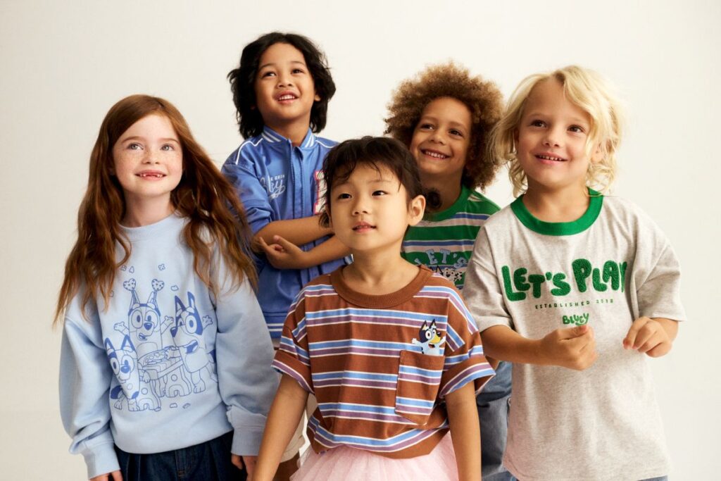 A cheerful group of children standing together wearing Bluey apparel, smiling for the camera.