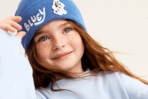 A young girl wearing a blue beanie smiles at the camera, showcasing her playful spirit.
