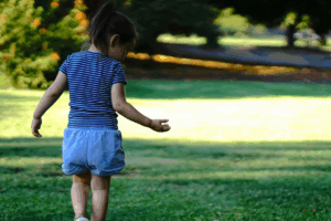 A little girl sits on a bench, laughing joyfully with her hands on her knees.