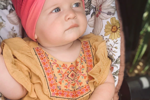 A baby in a pink hat sits comfortably in a stroller, smiling and enjoying the outdoors.
