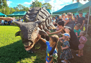 A group of children excitedly pet a friendly dinosaur at a lively event.