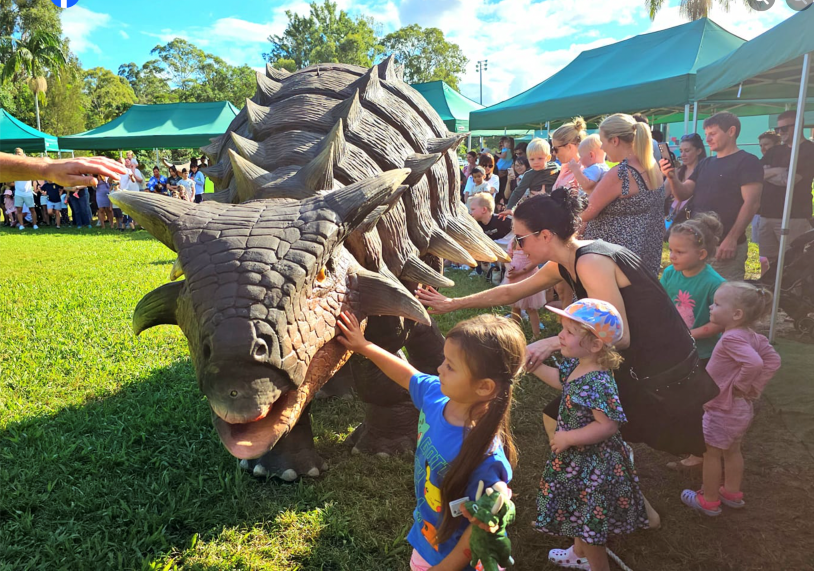 A group of children excitedly pet a friendly dinosaur at a lively event.