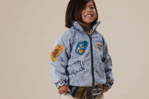 A young girl in a denim jacket adorned with colorful patches, smiling at the camera.