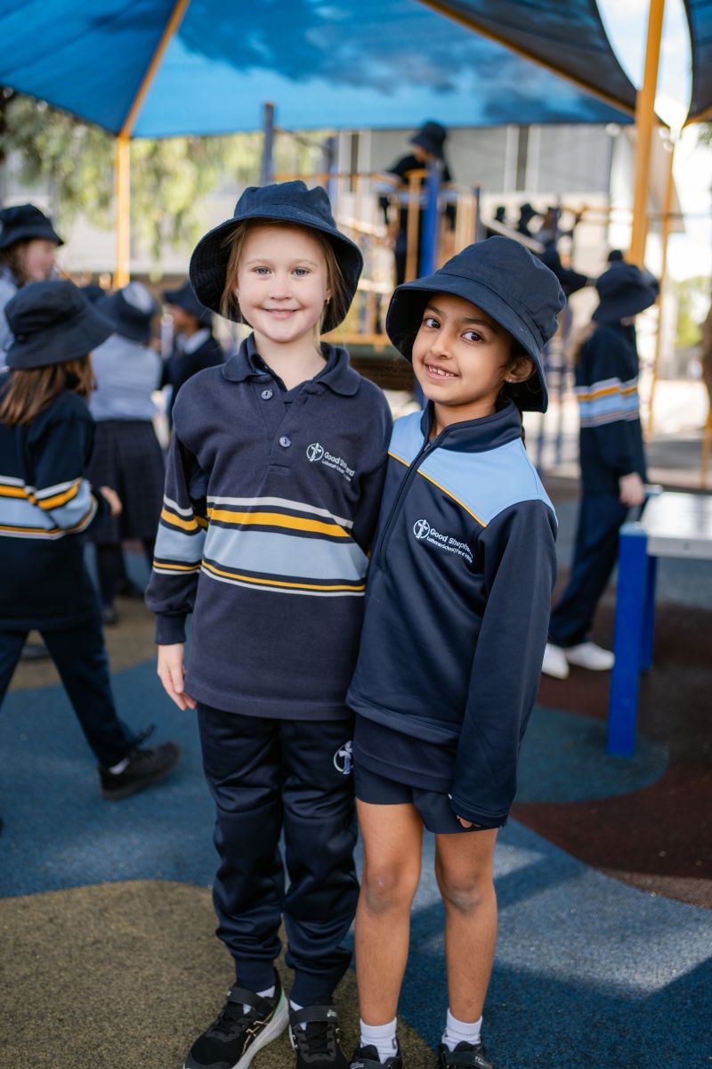 Two children in school uniforms stand together on a playground, smiling and enjoying their time outdoors.