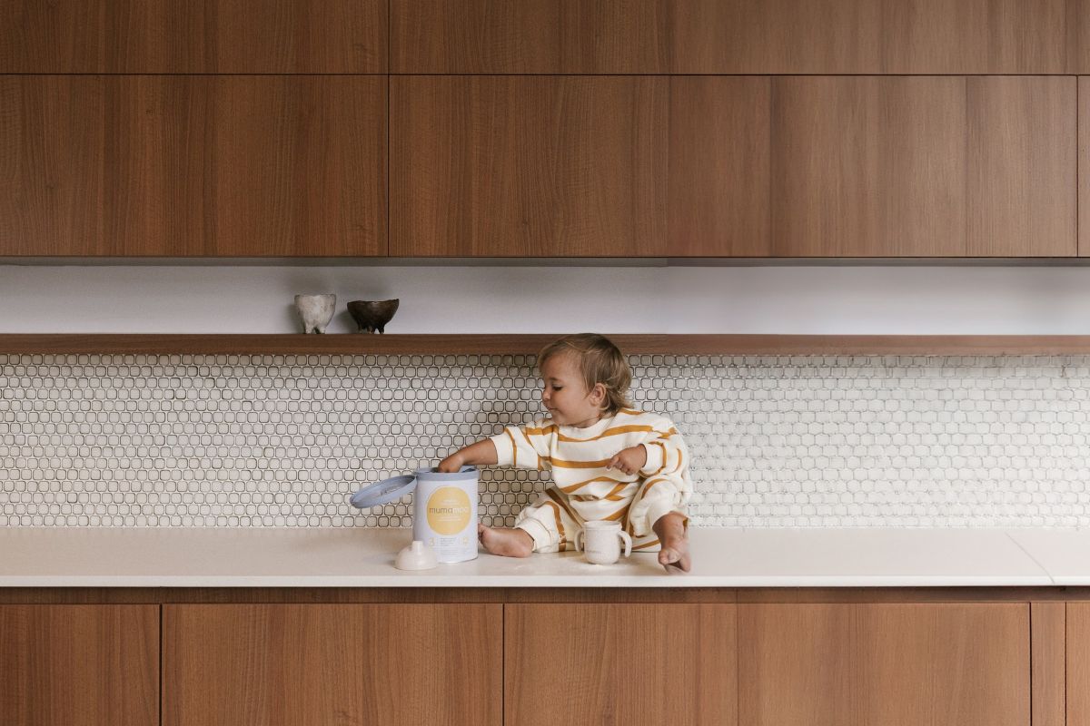A child sitting on a kitchen counter, smiling and playing with kitchen utensils.