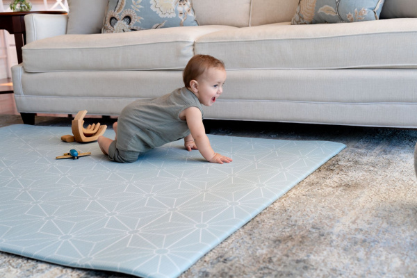 A baby crawling on a blue rug in front of a couch, exploring their surroundings with curiosity.