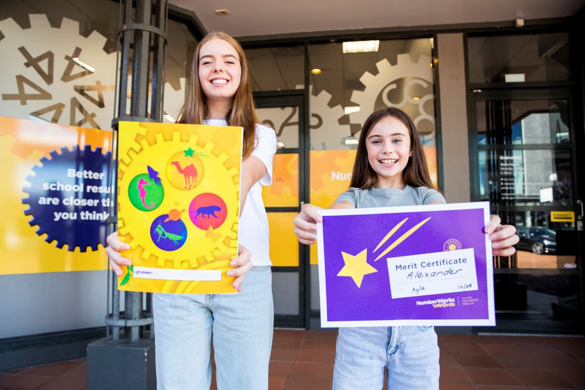 Two girls stand outside a building, proudly holding up colorful posters with messages.