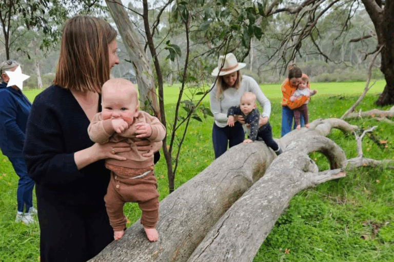 A woman and two children stand on a fallen tree, smiling and enjoying a sunny day in a forested area.