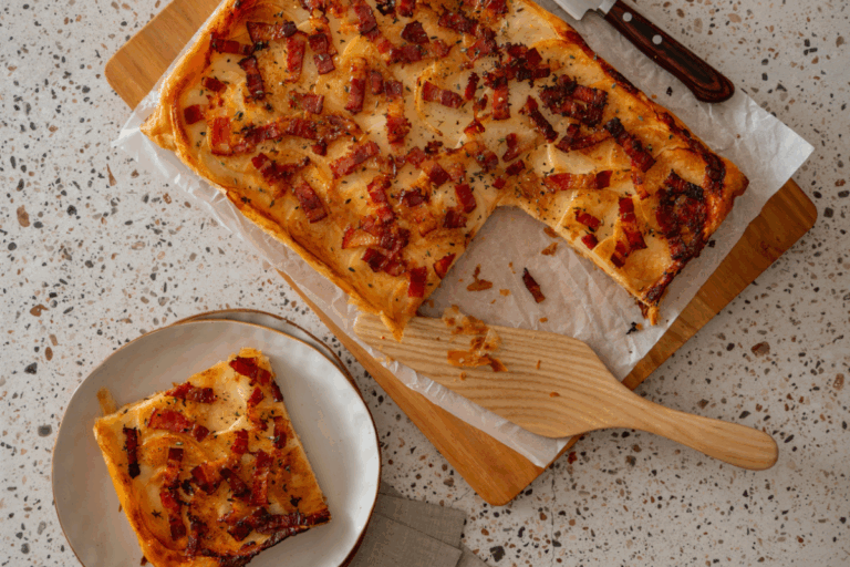 A slice of tart resting on a wooden cutting board, showcasing melted cheese and toppings.