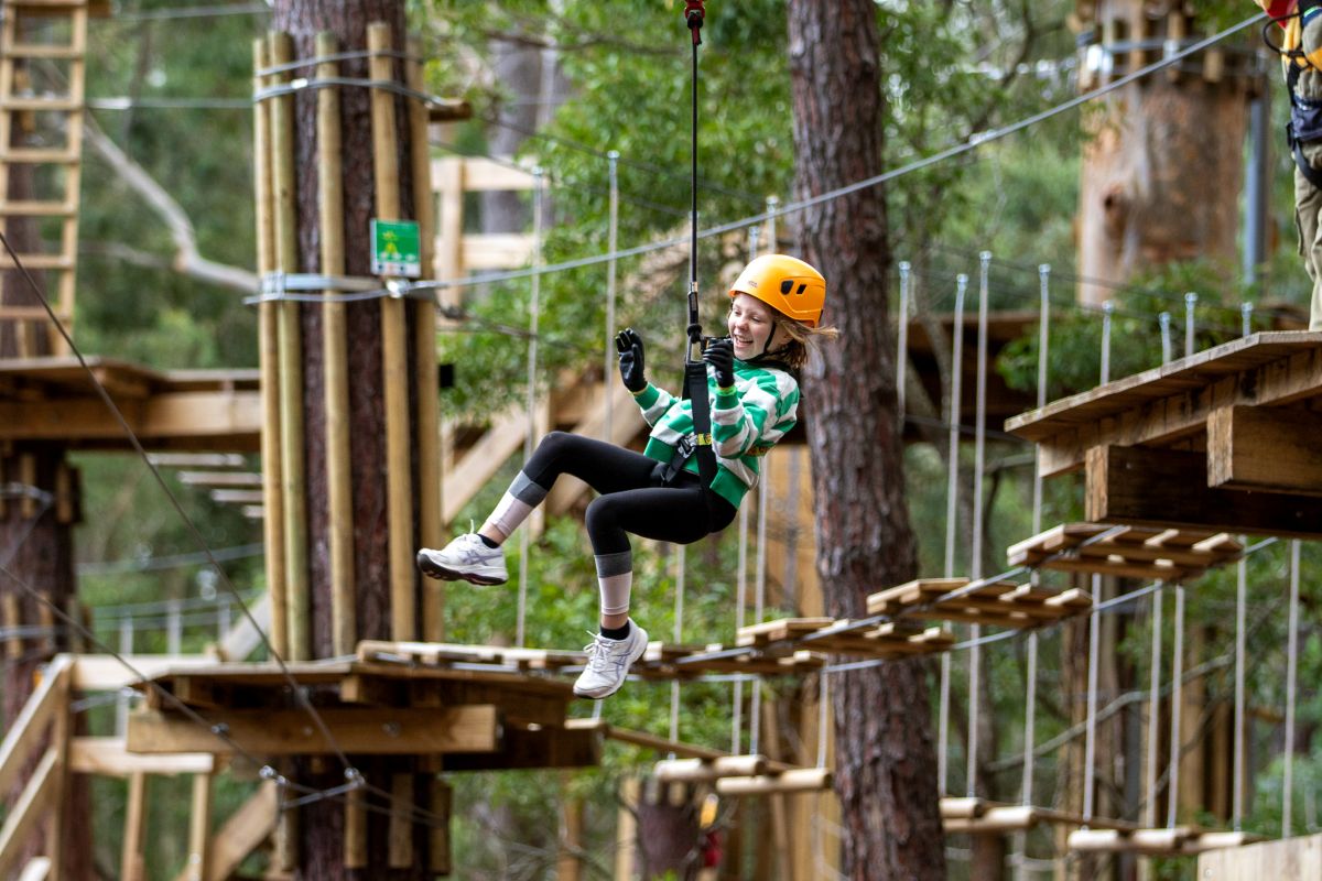 A young girl glides on a zip line through a lush green forest, enjoying an adventurous outdoor experience.