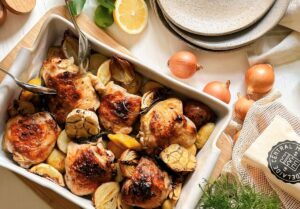 Baked chicken and potatoes seasoned with herbs in a rectangular dish.
