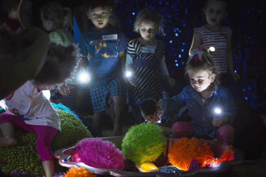 Children joyfully playing with colorful lights in a dimly lit room, creating a magical atmosphere.