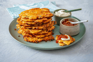 A plate stacked high with golden-brown potato pancakes, garnished and ready to be served.