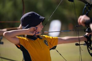 A young boy focuses intently as he aims his bow at a colorful archery target.