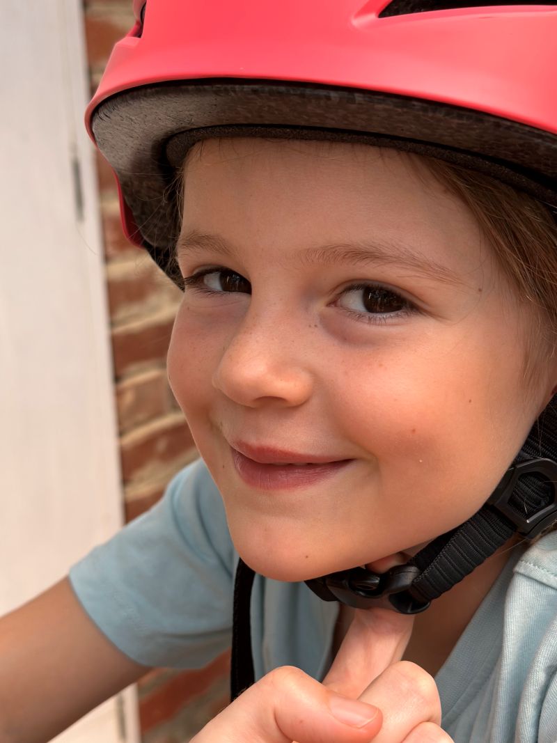 A child wearing a safety helmet, smiling and ready for an outdoor activity.
