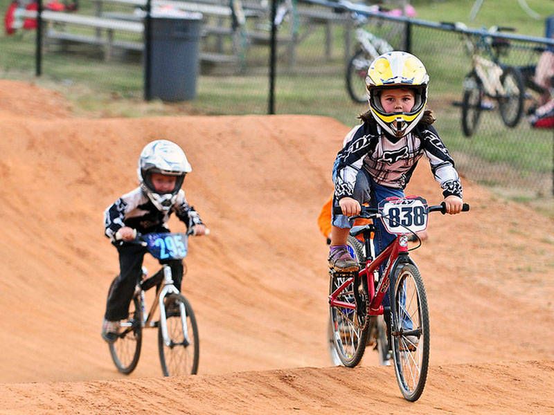 Two young children riding bikes on a dirt track, enjoying a sunny day outdoors.
