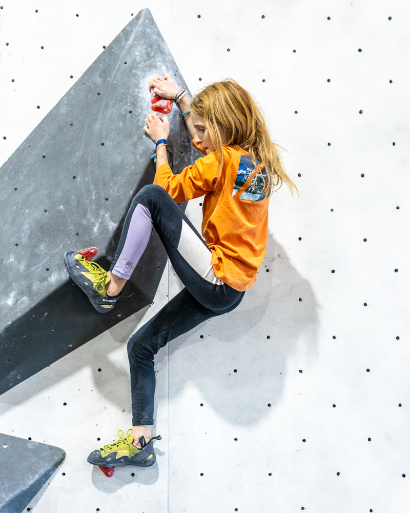 A young girl climbing a colorful rock wall, focused and determined as she reaches for the next hold.