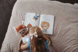 A young girl sits on a bed, engrossed in reading a book with a focused expression.
