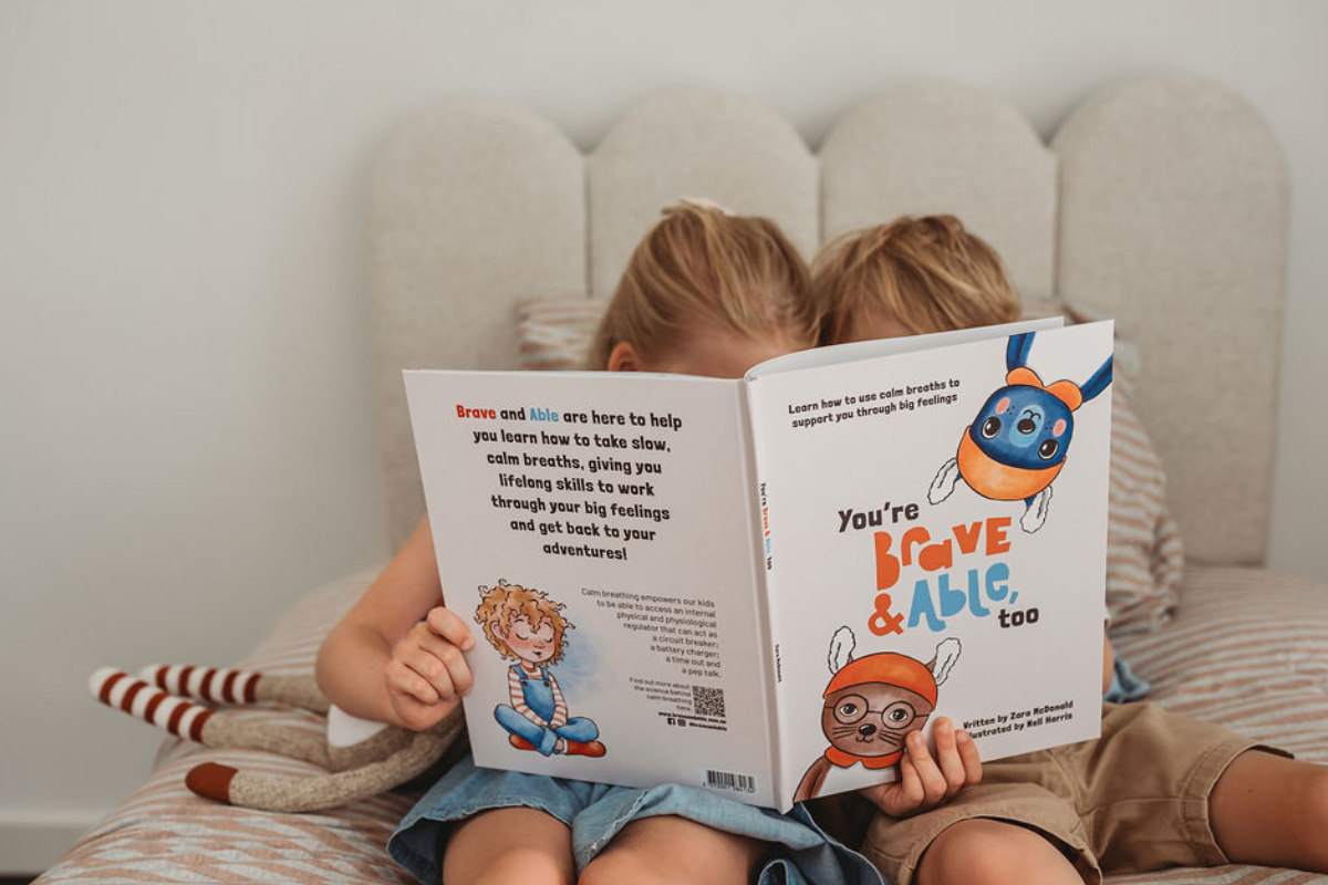 Two children sitting on a bed, engrossed in reading a colorful children's book together.