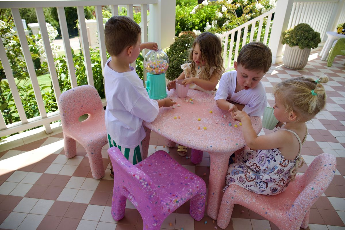Children playing together at a pink table surrounded by chairs, engaged in fun activities.