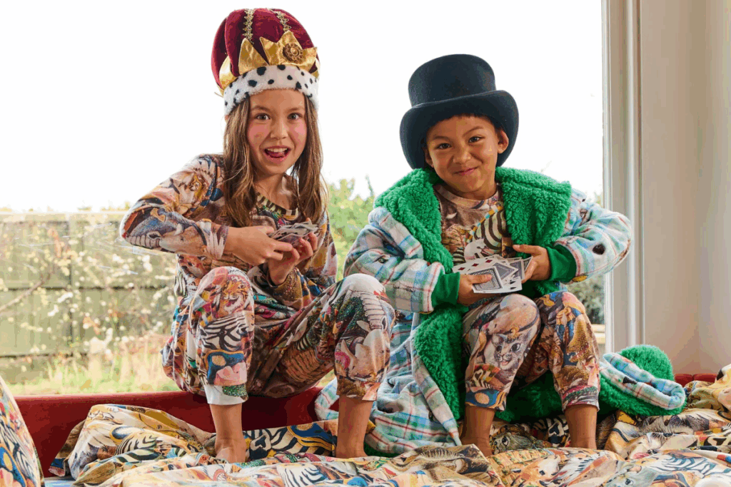 Two children in pajamas and hats sitting on a bed, smiling and enjoying a cozy moment together.