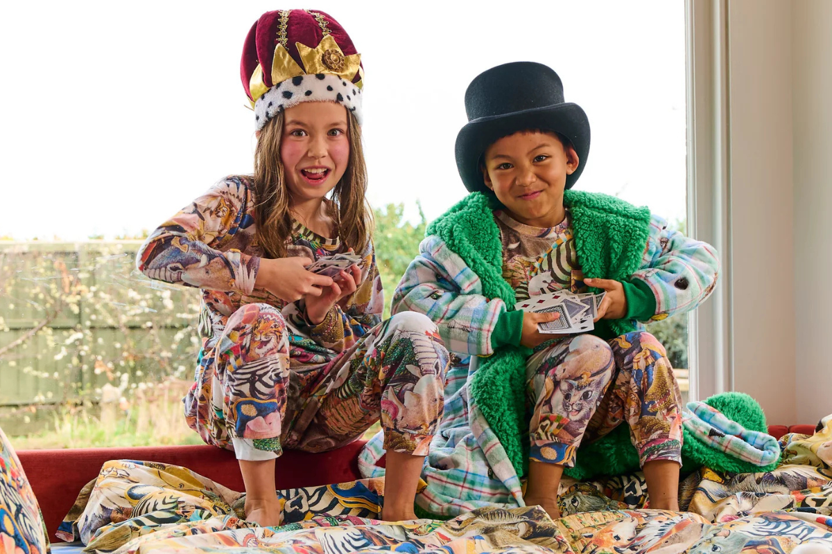 Two children in pajamas and hats sitting on a bed, smiling and enjoying a cozy moment together.