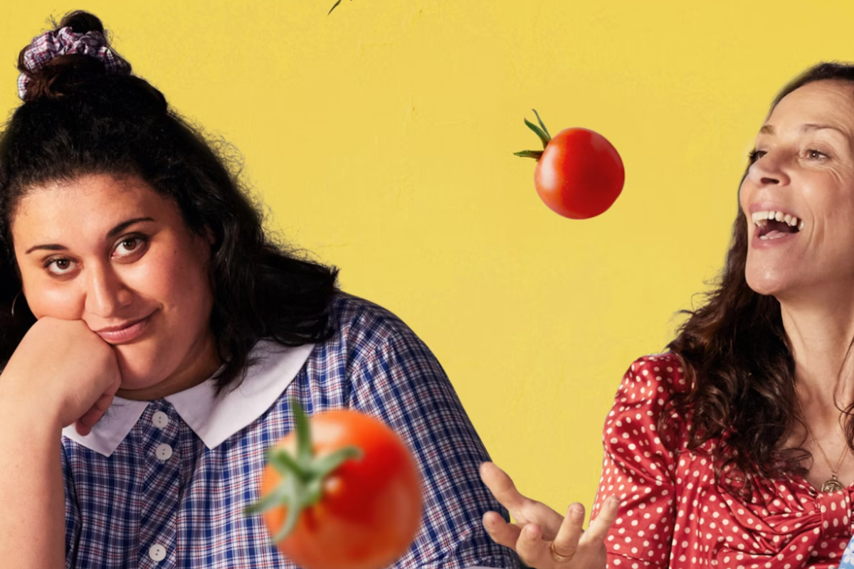  Two women sit against a yellow background as tomatoes fly through the air around them.