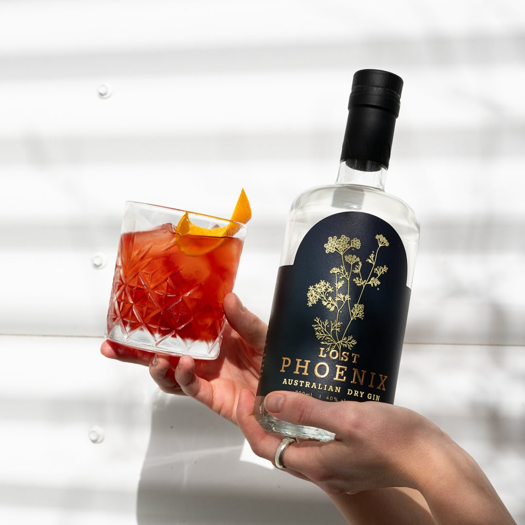 A hand holds a bottle of gin alongside a glass.