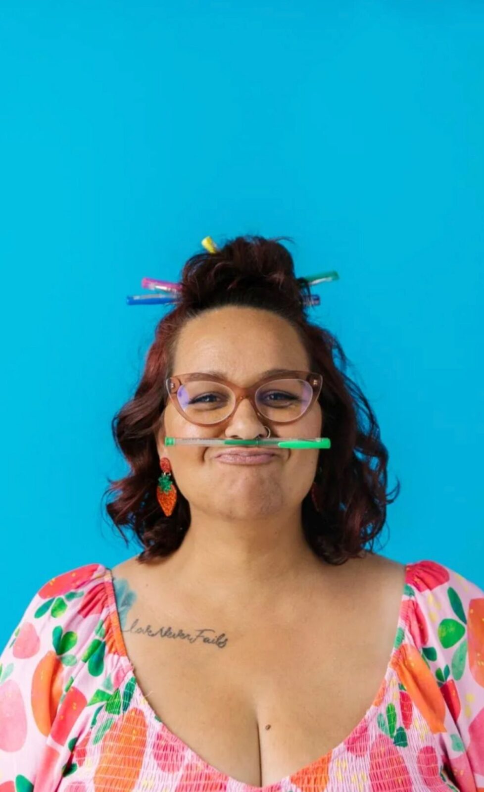 A woman playfully holds a pencil in her mouth, looking thoughtful while working on a project.