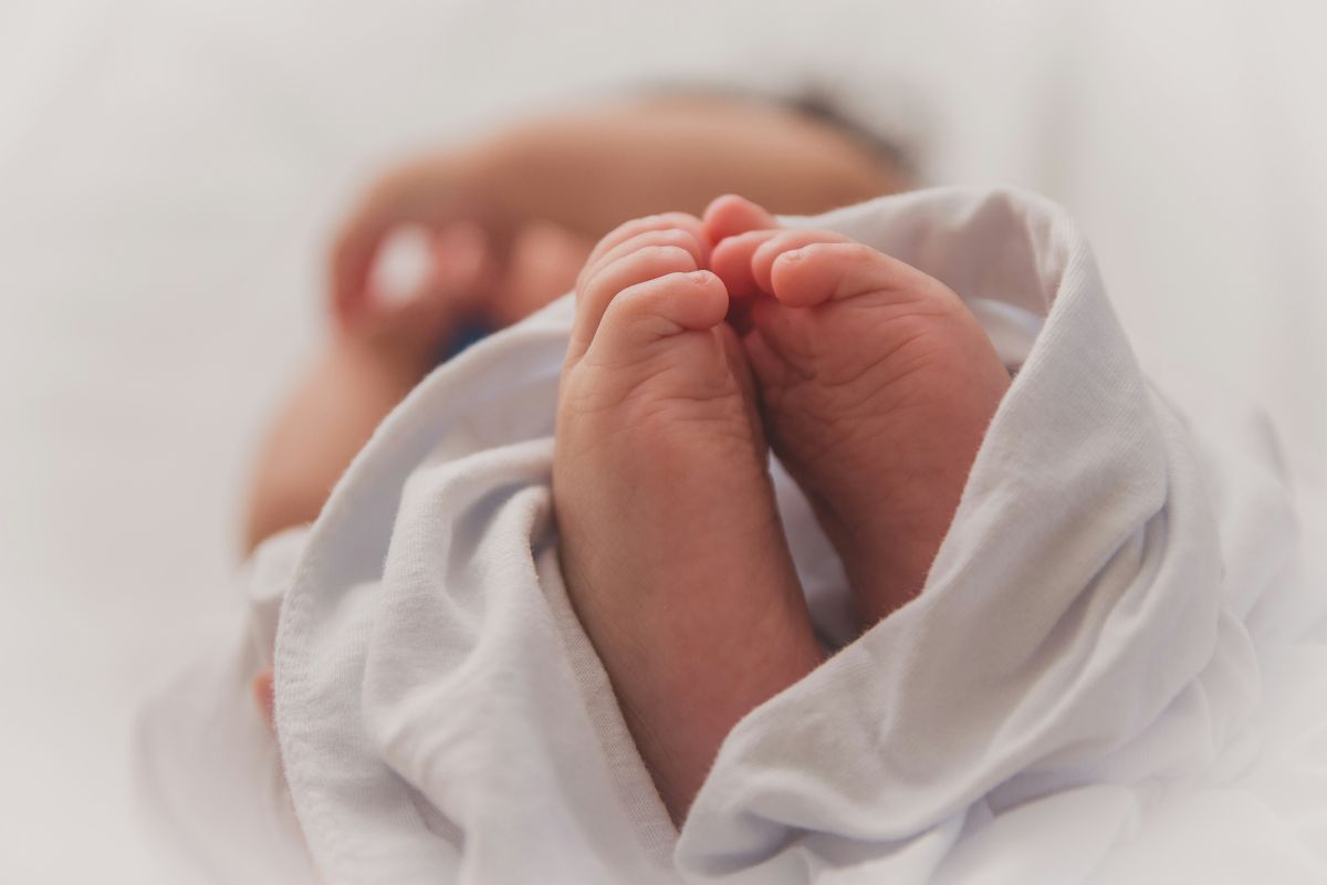 A close-up of a newborn baby's feet resting on soft white sheets.