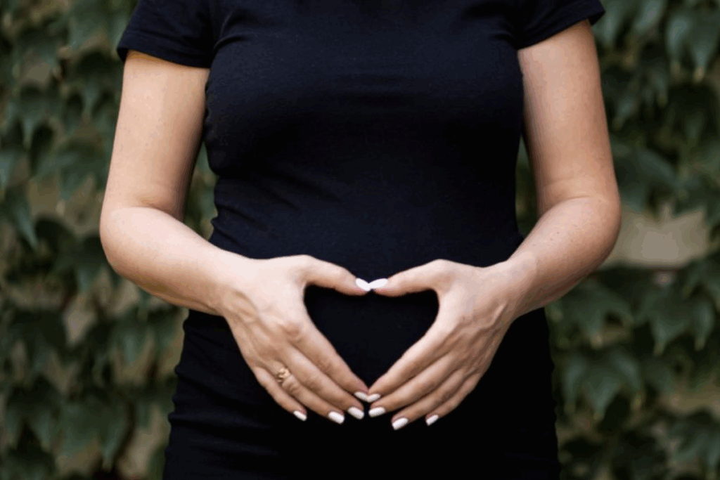 A pregnant woman forms a heart shape with her hands, smiling gently, showcasing her joy and anticipation of motherhood.